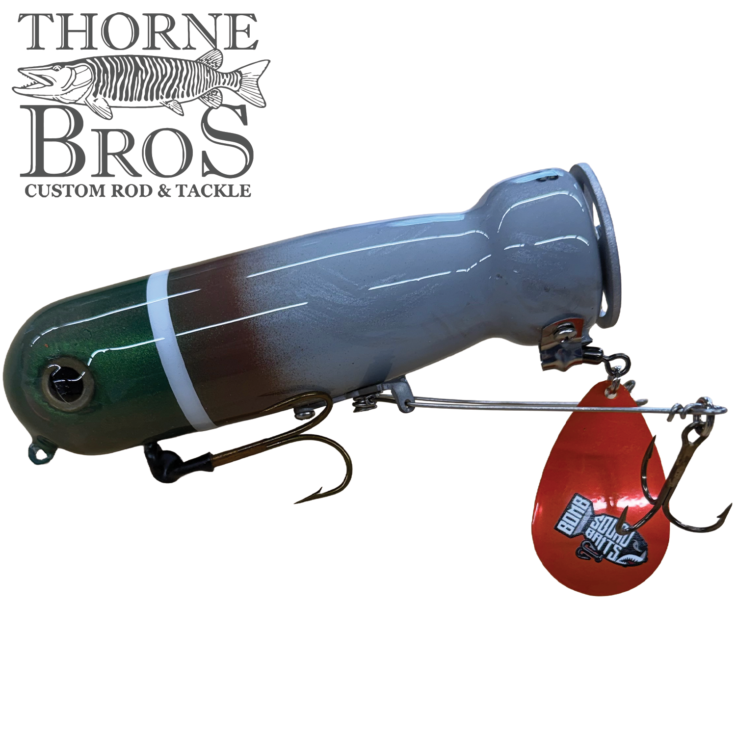 Bomb Squad MK-65 Flap Tail musky fishing lure with green, brown, and white body, featuring sharp hooks and a red metal flap spinner for added water attraction.