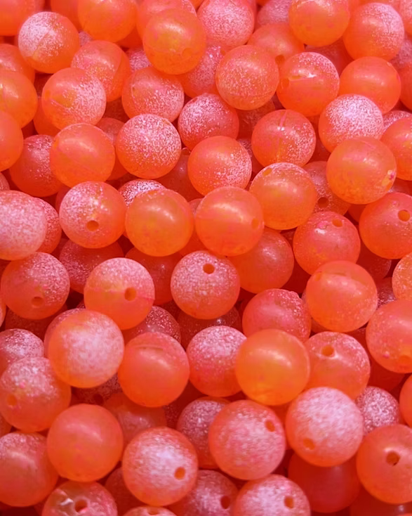 Close-up image of multiple small, round, translucent orange beads with a matte finish and tiny holes through the center, used for fishing tackle by Bloop Bead Co.
