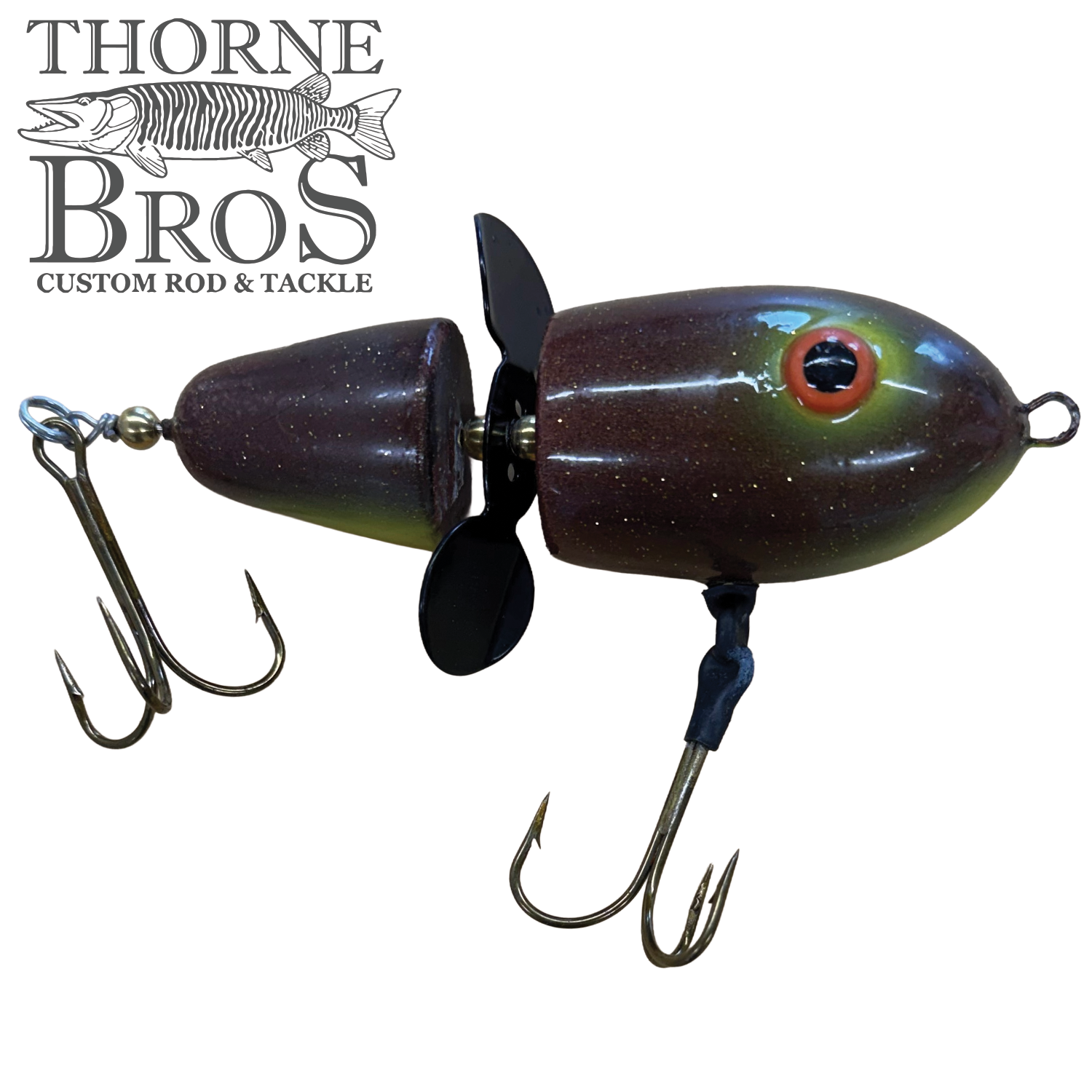Close-up of a dark brown, segmented fishing lure with dual treble hooks and a black propeller, designed for musky fishing, identified as Lake-X Hammer.