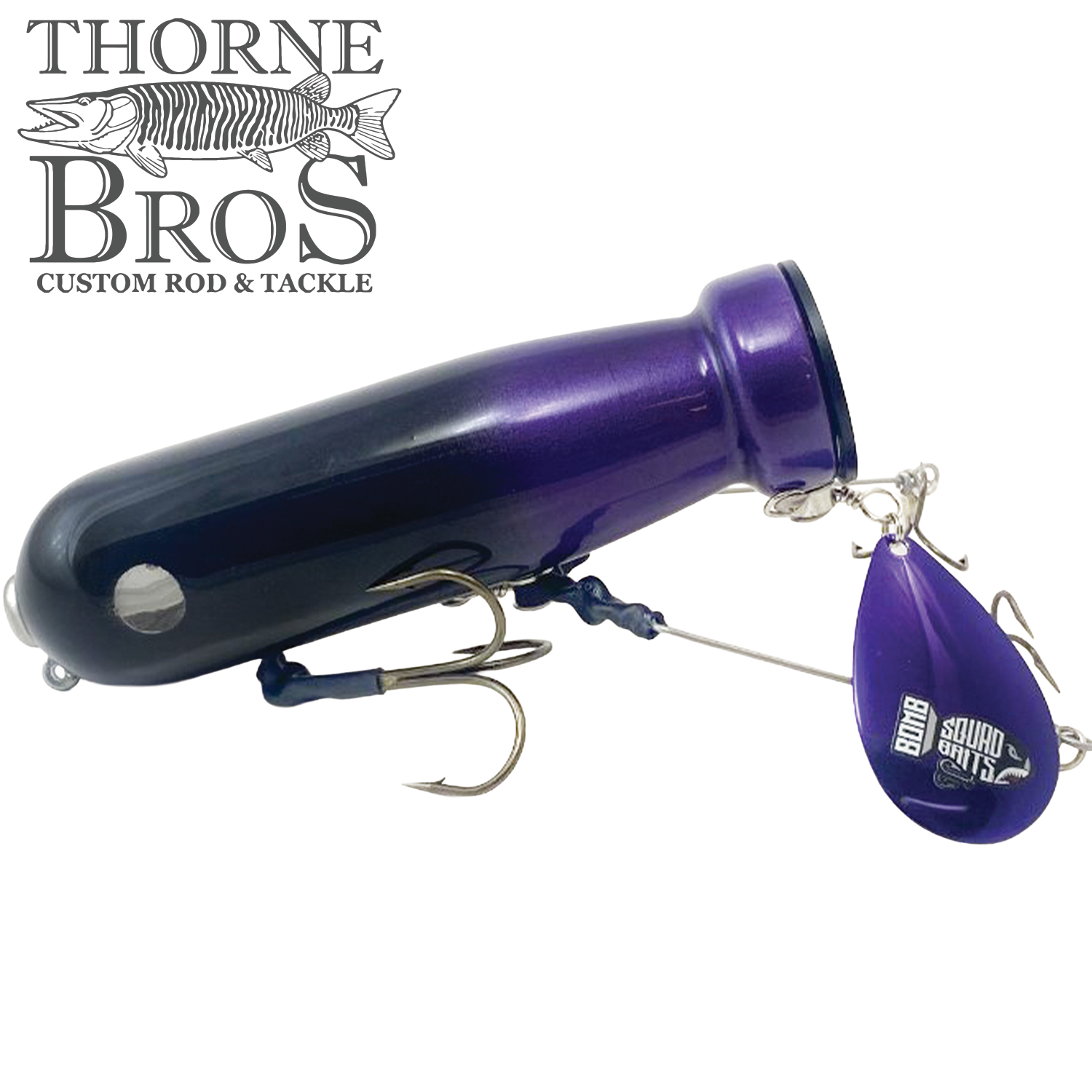 Bomb Squad MK-65 Flap Tail fishing lure in purple with a large body, dual treble hooks, and a spinning flap tail designed for musky fishing.