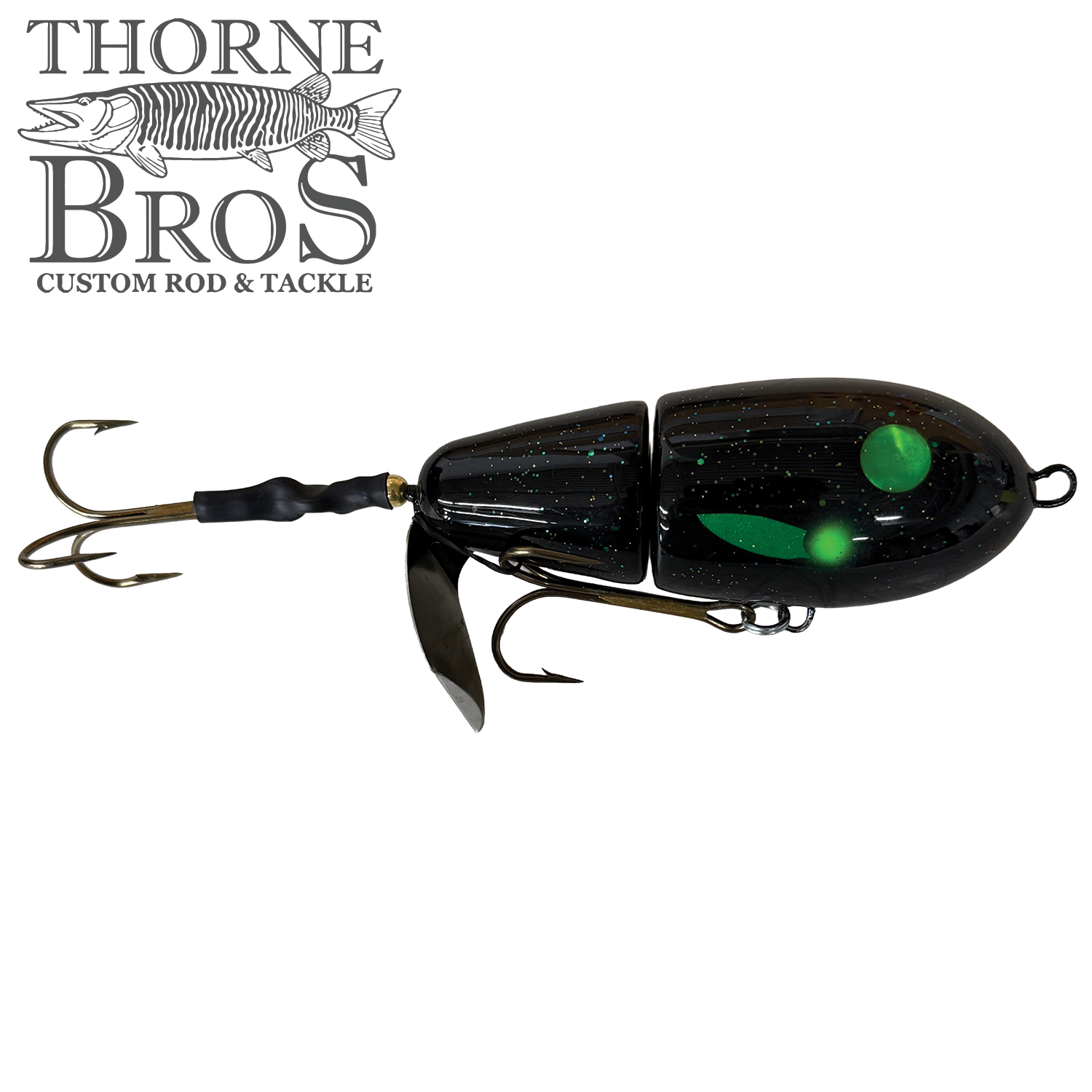 Lake-X Fat Bastard fishing lure in black with green glowing spots, featuring dual treble hooks and a metal spinner blade for musky fishing.