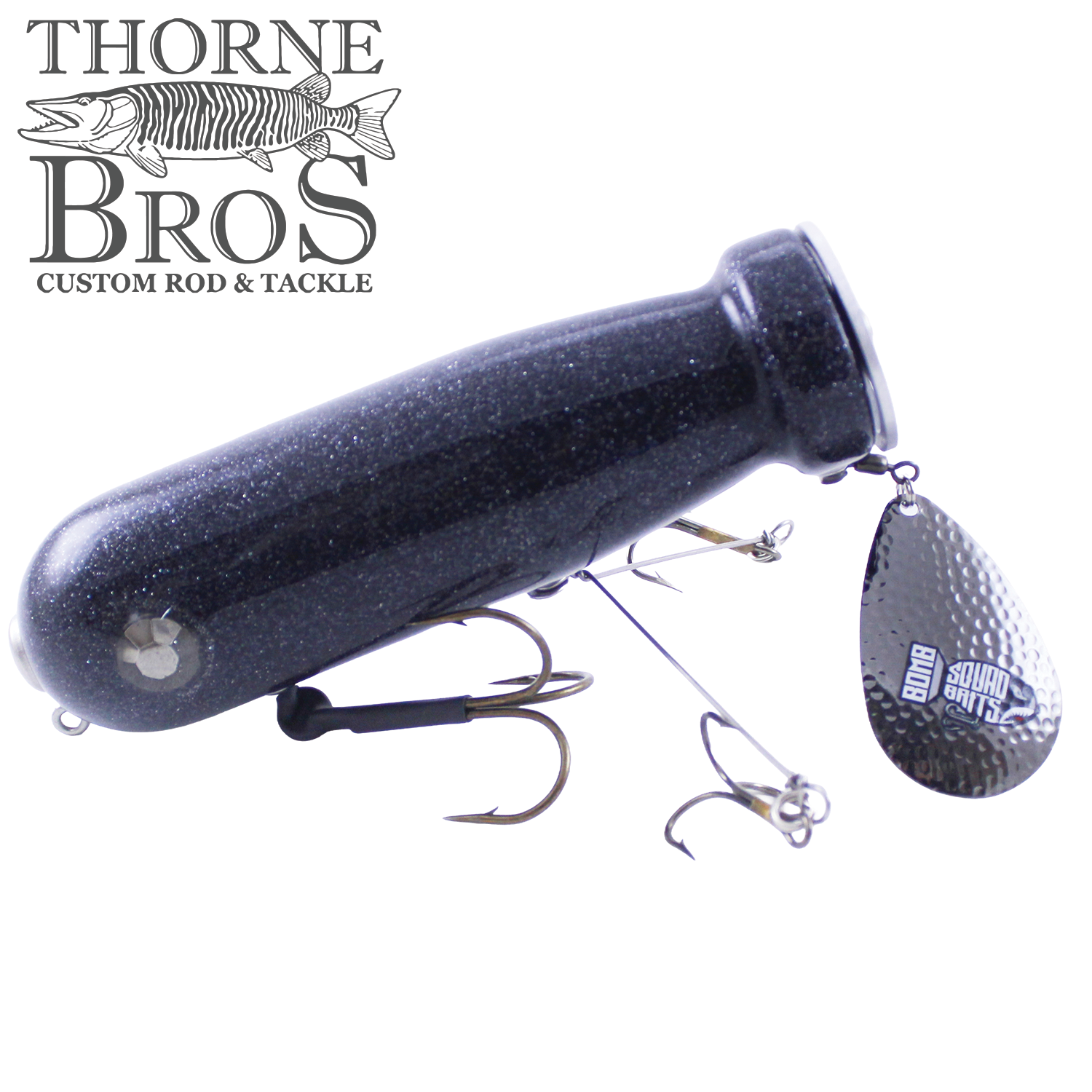 Bomb Squad MK-65 Flap Tail fishing lure with a dark, speckled body, equipped with multiple treble hooks and a textured metallic flap tail spinner for musky fishing.