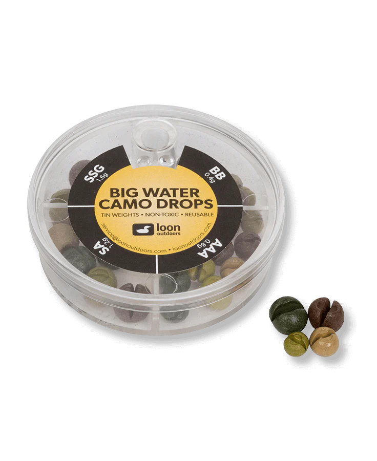 Clear plastic circular container of Loon Tin Drop Assortments with camo-colored fishing weights in multiple sizes, showing a variety of green, brown, and tan tones designed for fishing tackle use.