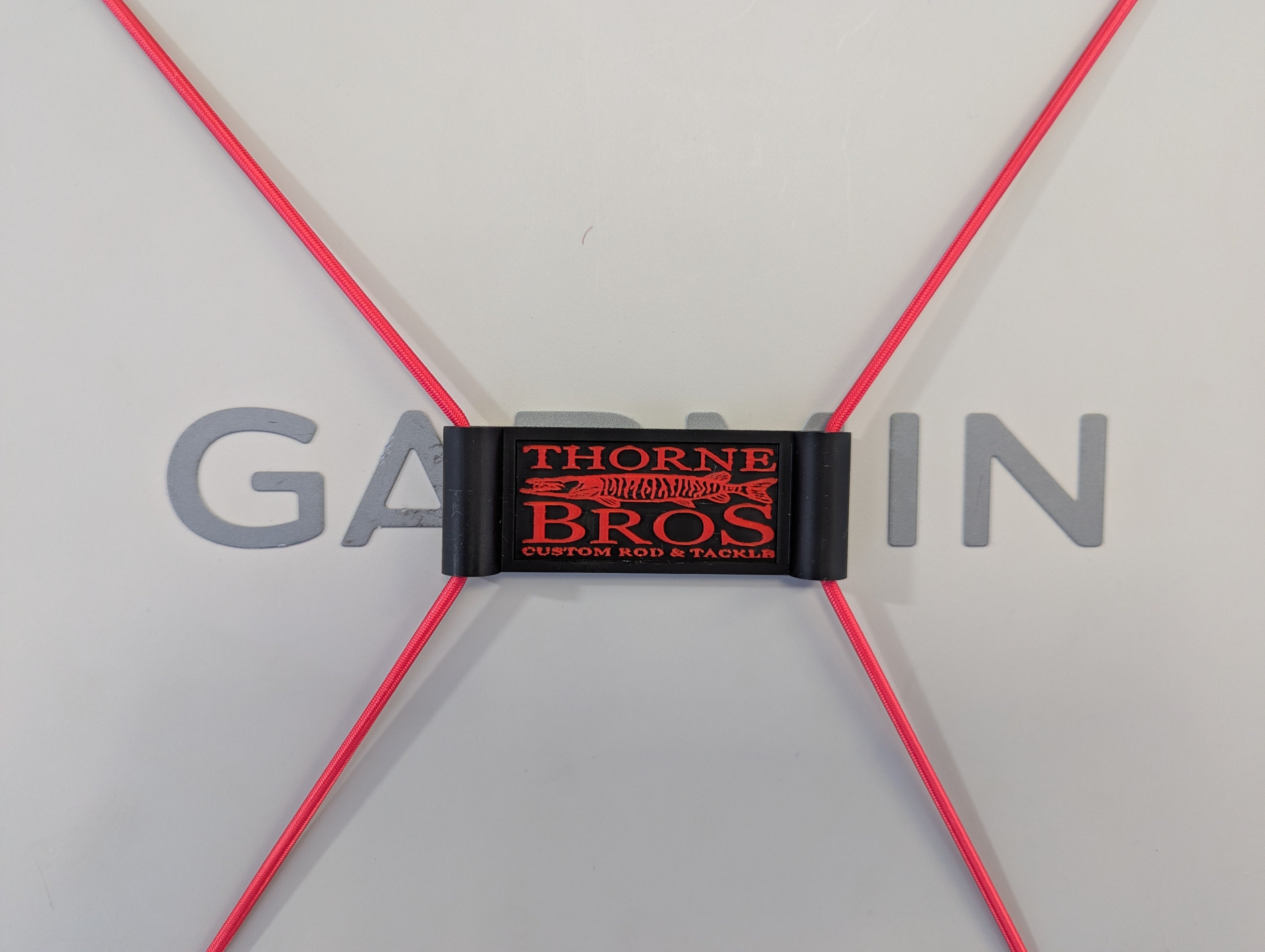Thorne Bros Graph Cover Strap in black with red logo, designed to secure fishing rods and tackle, shown holding bright red cords against a light background.