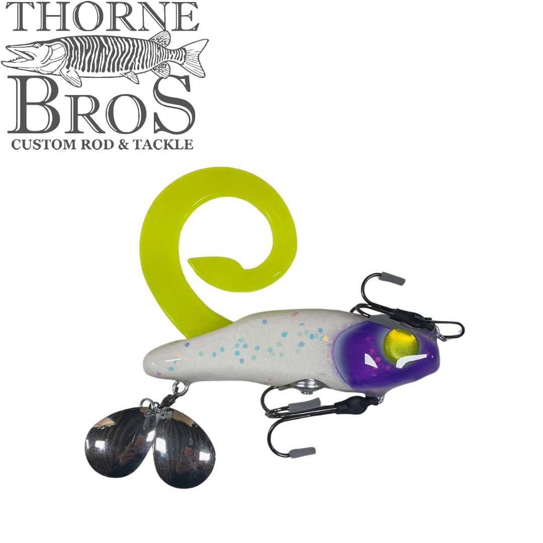 Zilla Baits Gladiator (Mini & Standard) fishing lure with a curved bright yellow tail, white body with blue speckles, purple head, and metal spinner blades for attracting fish.