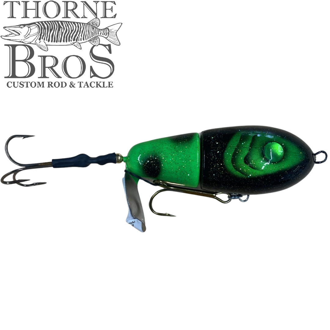 Lake-X Fat Bastard (Epoxy Finish) fishing lure in green and black with two treble hooks and a metal spinner blade, designed for musky fishing tackle.