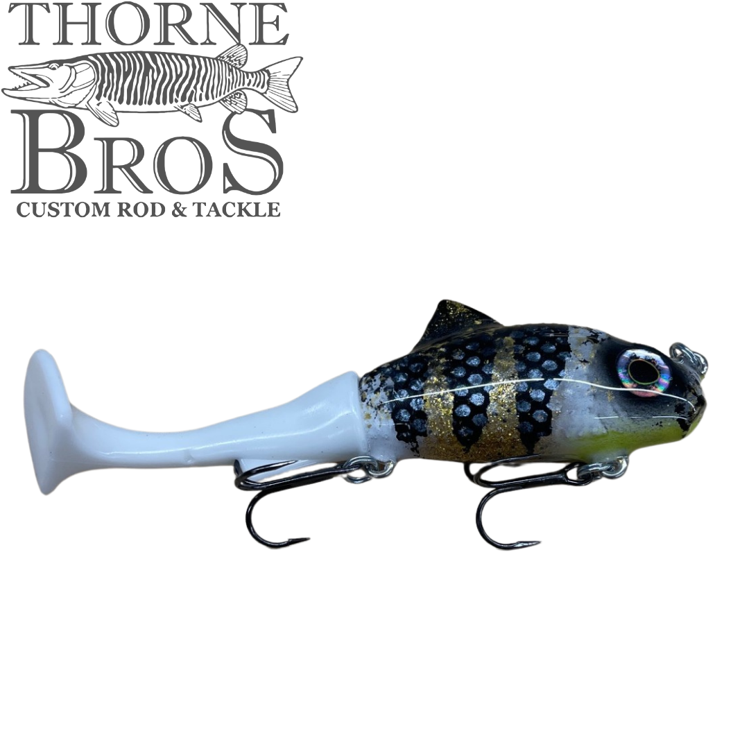 Zilla Baits TicTak soft plastic musky fishing lure with blue gray body black markings treble hooks and paddle tail beside the Thorne Bros logo