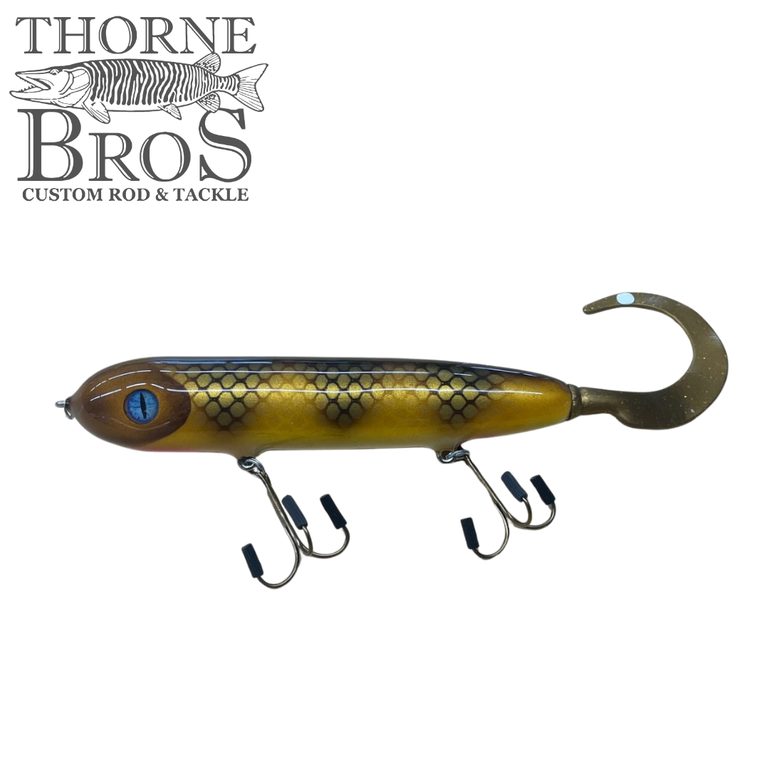 Holmgren Serpent Musky Top Water fishing lure with a gold and black scaled body, lifelike blue eye, and a curly tail designed for musky fishing.
