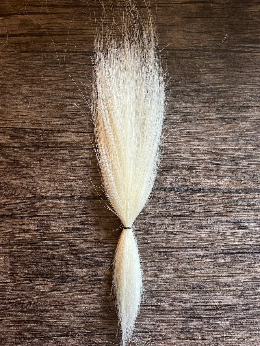 Close-up of a bundle of fine, white and light cream synthetic fibers tied together, used as fishing tackle material for the Squimpish Sparkle Blend lure.