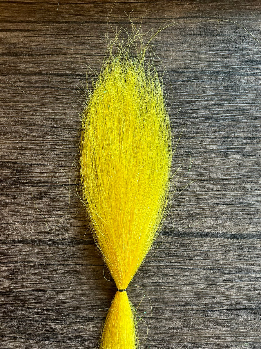 Bright yellow synthetic fishing lure material bundle secured with a black tie, shown on a wooden surface, designed for creating the Squimpish Sparkle Blend fishing tackle.