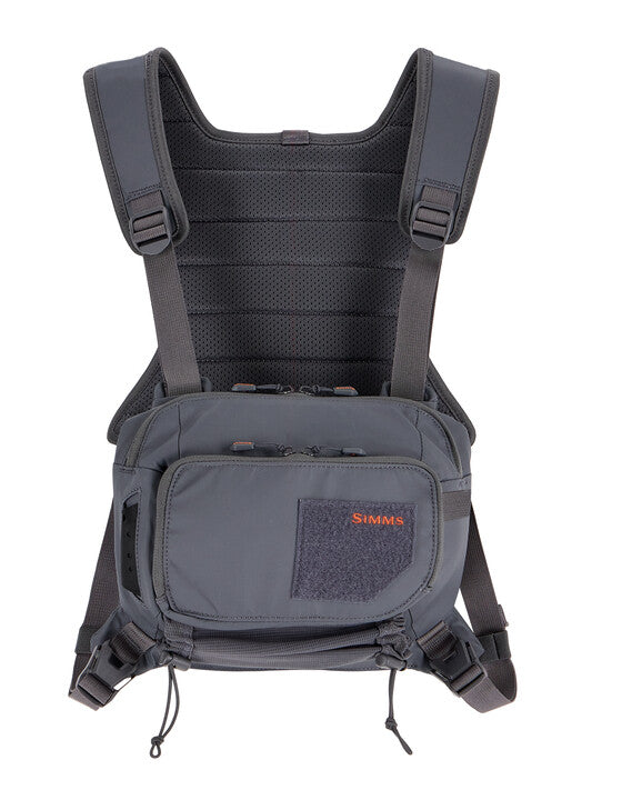 Simms Tributary Chest Pack in dark gray with adjustable padded shoulder straps, multiple zippered compartments, and front patch for secure storage while fishing.