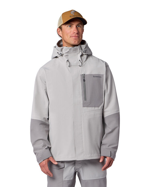Man wearing a light gray Simms Men's Challenger Rain Jacket with a hood and zippered chest pocket, paired with matching pants and a beige cap, suitable for fishing or outdoor activities.