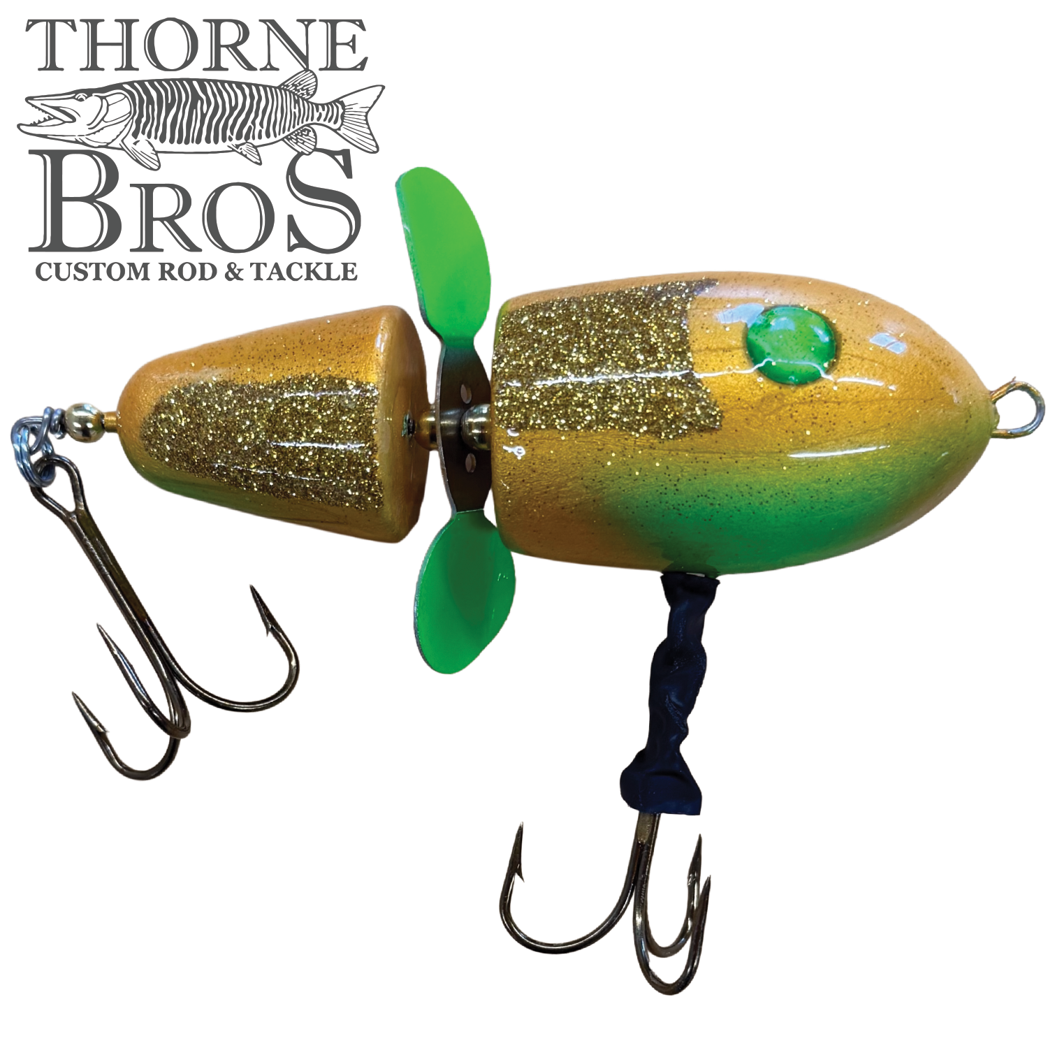 Close-up of the Lake-X Hammer fishing lure featuring a segmented wooden body painted gold and green with glitter accents, equipped with two treble hooks and a green propeller for musky fishing.