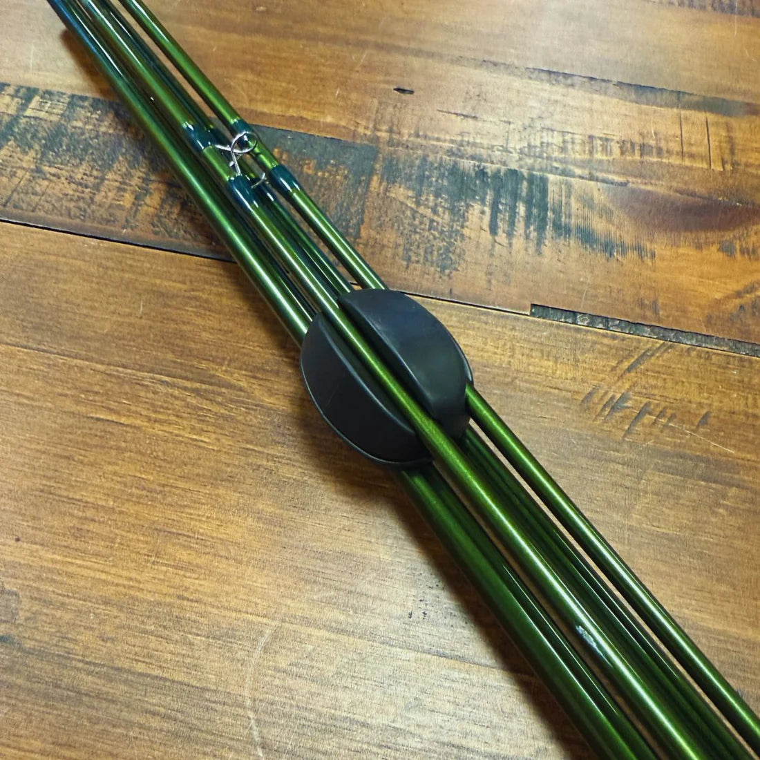 Trxstle Flex-Lock Silicone Rod Keeper securing bundled green fishing rods on a wood surface for organized transport and storage