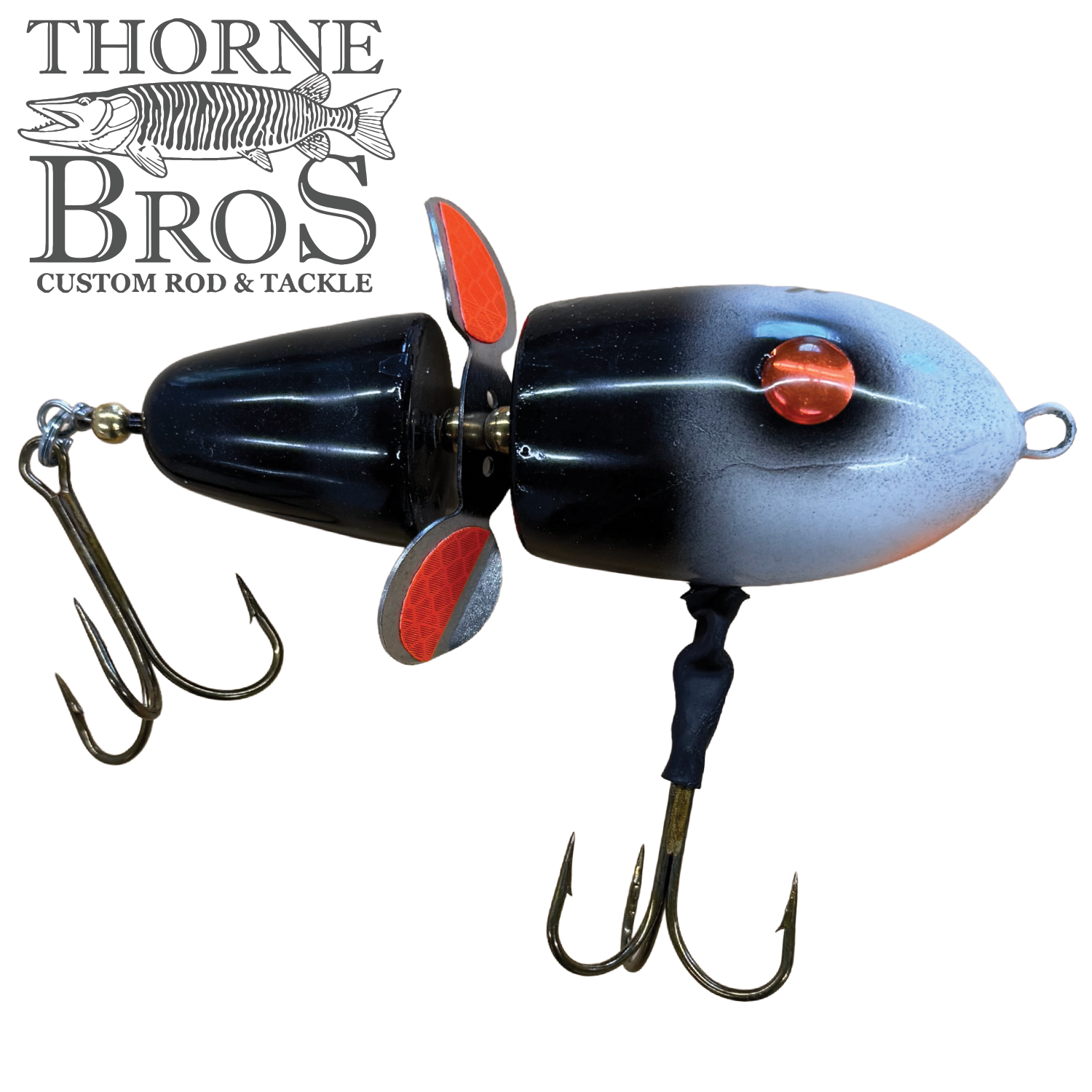 Close-up of a Lake-X Hammer fishing lure featuring a segmented black and gray body with red eyes, two treble hooks, and metal spinning blades for musky fishing.