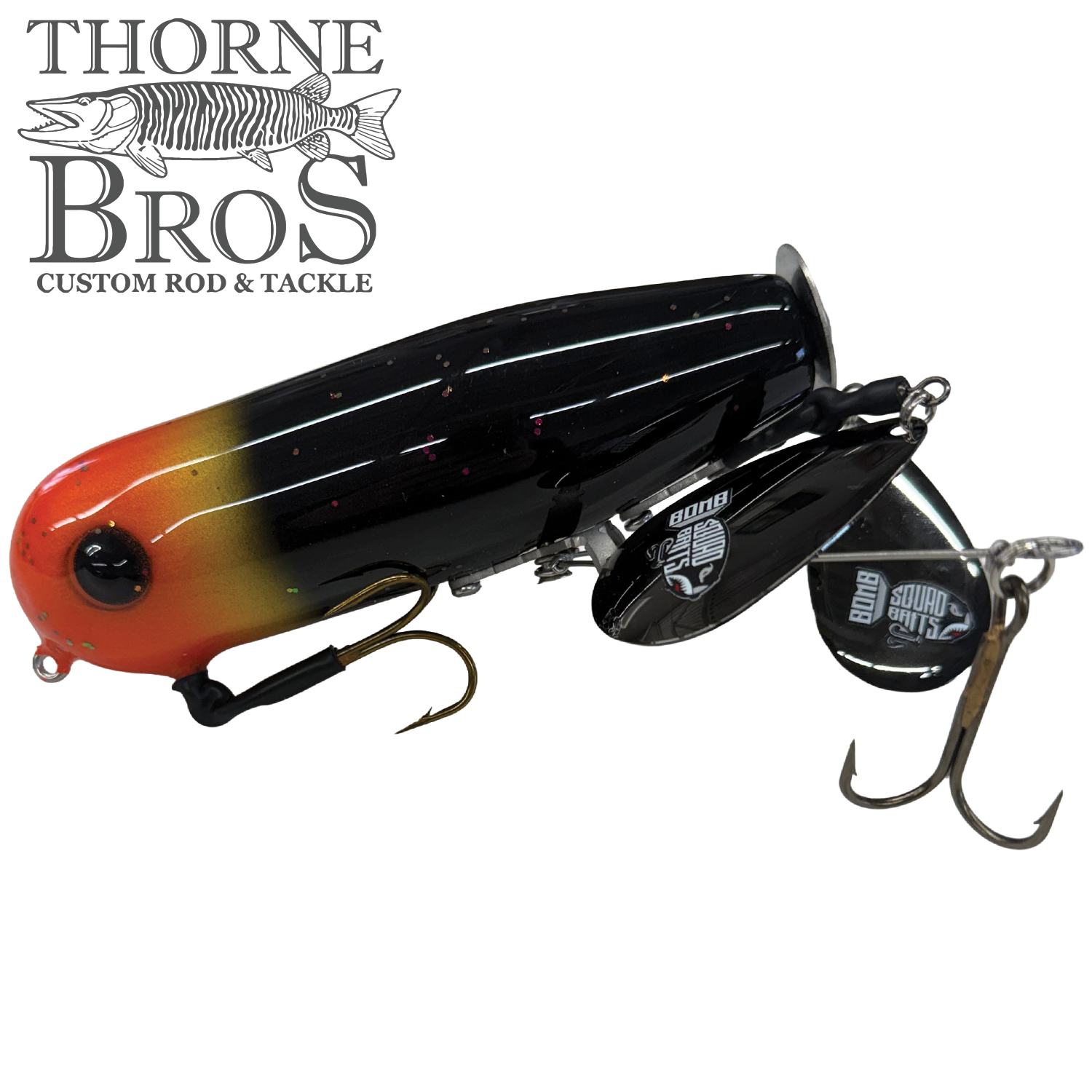 Bomb Squad Double Tap Flap Tail fishing lure with black and orange gradient body, detailed eyes, dual treble hooks, and metal spinning blades, designed for musky fishing.