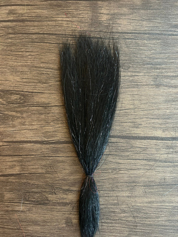 Black synthetic fishing lure material with subtle sparkle strands laid out on a wooden surface, designed for use with Squimpish Sparkle Blend fishing tackle.