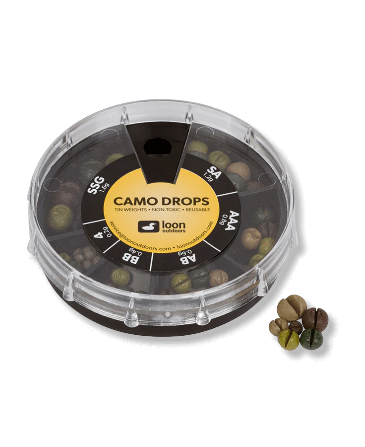 Clear round plastic container with multiple compartments holding small camo-colored tin weights labeled Loon Tin Drop Assortments, accompanied by a close-up of varied green, brown, and tan fishing tackle weights.