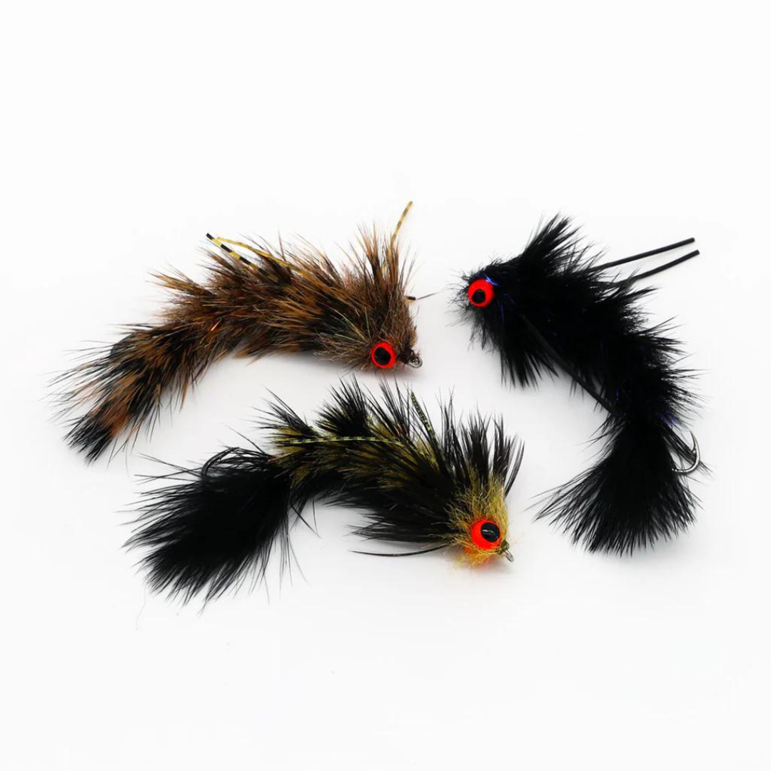 Three detailed Flymen Next Woolly Bugger Changer fishing lures with feathered bodies and bright red eyes arranged on a white background for fishing tackle use.