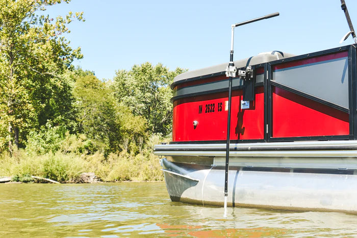 Red pontoon boat on a lake with a mounted Beatdown Outdoors Pontoon - Fixed Transducer Pole SKU:TPOLE-FIXED-AT-PONTOON attached to its side, surrounded by trees and calm water.