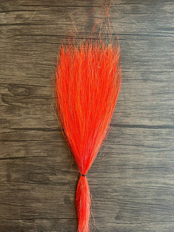 Bright orange synthetic fibers bundle tied at the base, designed for use in fishing tackle, shown against a wooden surface to highlight the Squimpish Sparkle Blend material.