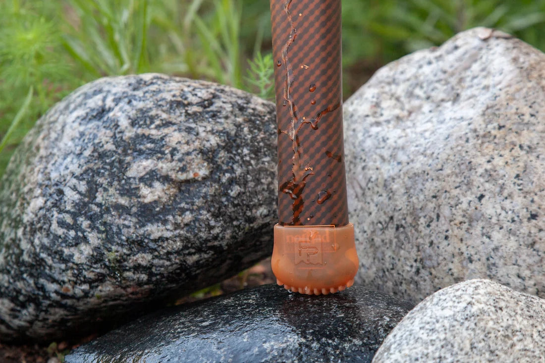 Fishpond Nomad End-Cap on a brown fishing rod handle resting among smooth granite rocks outdoors in a natural setting