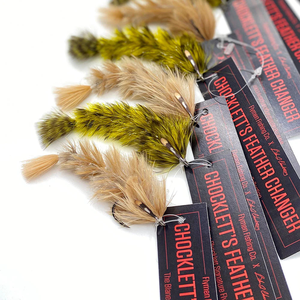 Close-up of multiple Chocklett's Feather Game Changer fishing lures featuring detailed feather designs in green and tan hues, attached to black tags with red and white text.