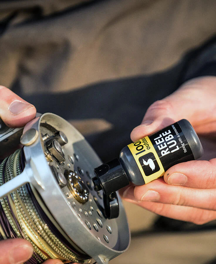Person applying Loon Outdoors Reel Lube oil to a fishing reel for maintenance, enhancing smooth performance of fishing rods and reels in outdoor use.