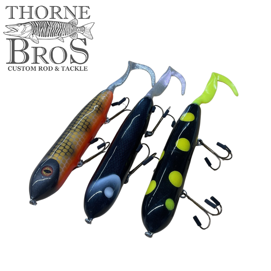 Three Holmgren Serpent Musky Top Water fishing lures in different colors, featuring curved tails and multiple treble hooks, displayed on a white background with Thorne Bros logo.