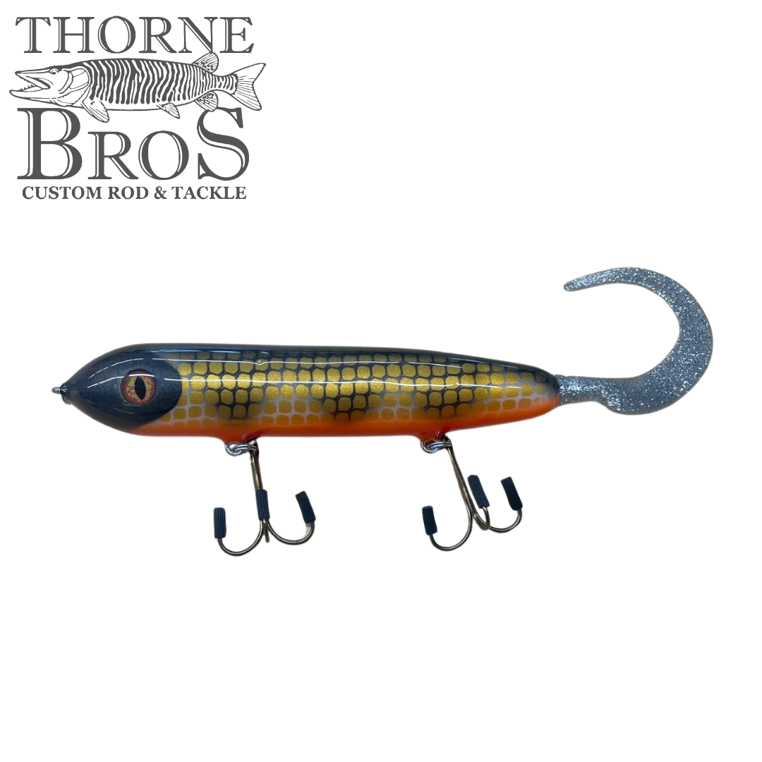 Holmgren Serpent Musky Top Water fishing lure with a detailed gold and black scaled body, orange belly, realistic eye, and a silver glittered curly tail designed for musky fishing.