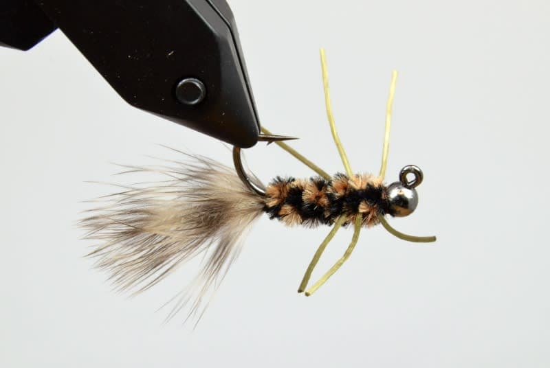 Close-up of a detailed fishing lure with a feathered tail and segmented body held in a vise, designed for use with "T.J. Hooker" fishing tackle.