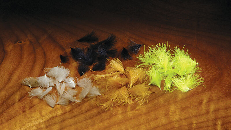 Hareline CDC Oiler Puffs in various colors including beige, black, orange, and bright yellow, displayed on a wooden surface, used as fishing tackle for fly fishing.