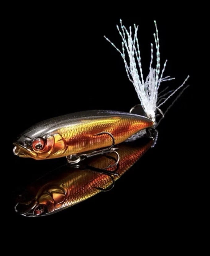 Megabass Karashi fishing lure with a sleek gold and black body, realistic fish scale texture, red eyes, dual treble hooks, and white feathered tail detail designed for musky fishing.