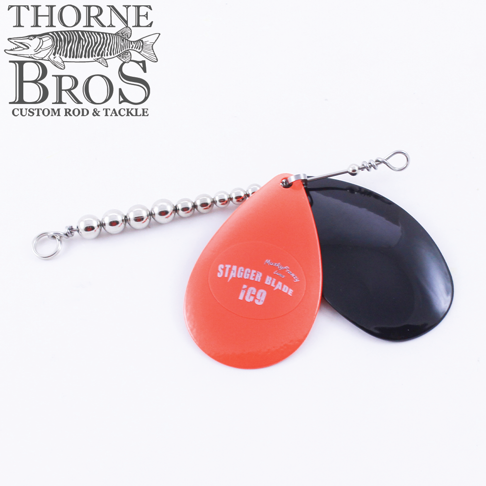 Musky Frenzy Blade Attachments featuring two curved fishing blades, one bright orange marked "Stagger Blade ic9" and one solid black, connected by a metal wire with silver beads for musky fishing tackle.